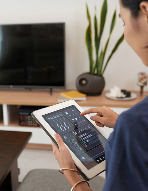 Pic showing a young woman controlling the sound on a home cinema system using an iPad